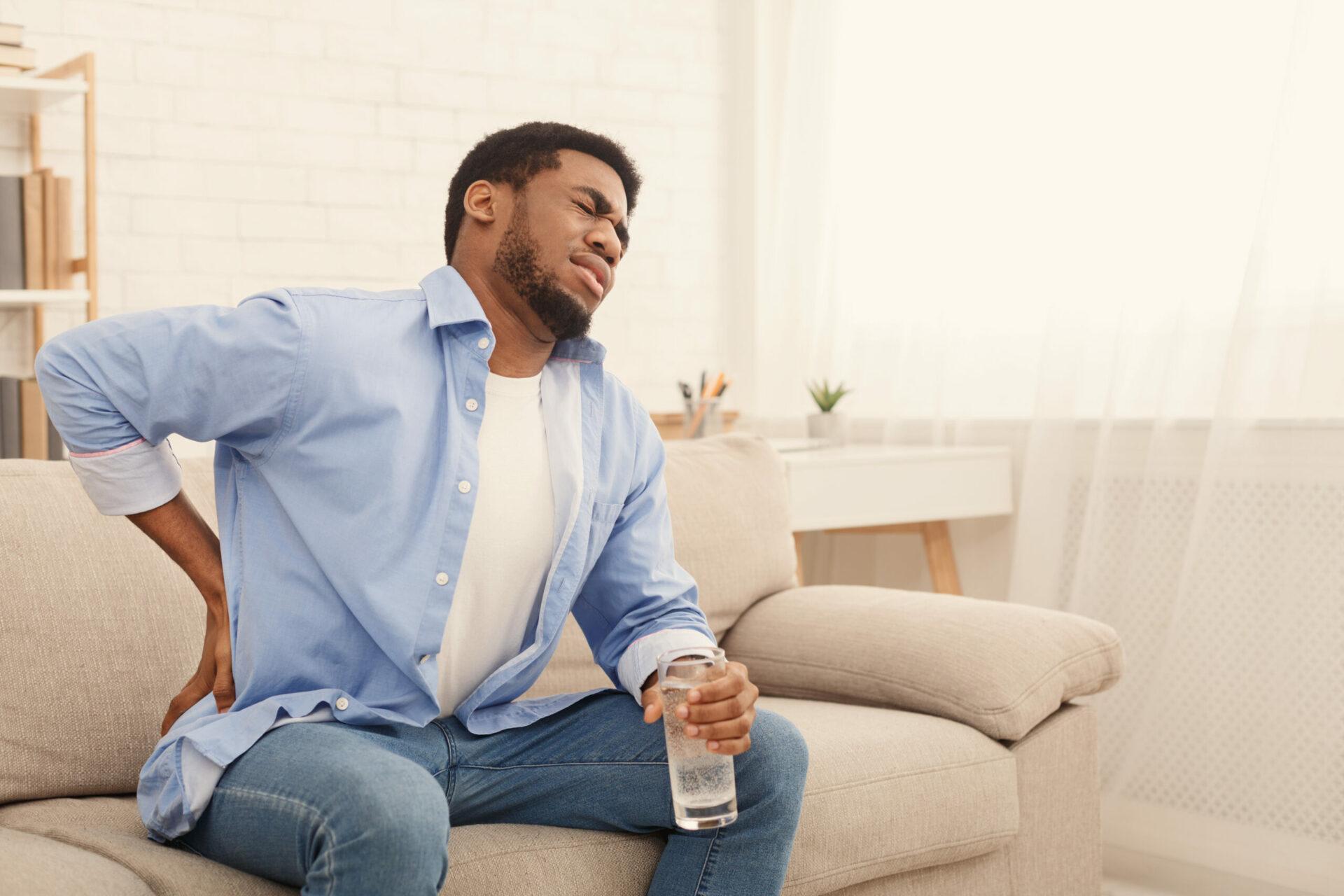 Man with back pain holding glass of water at home