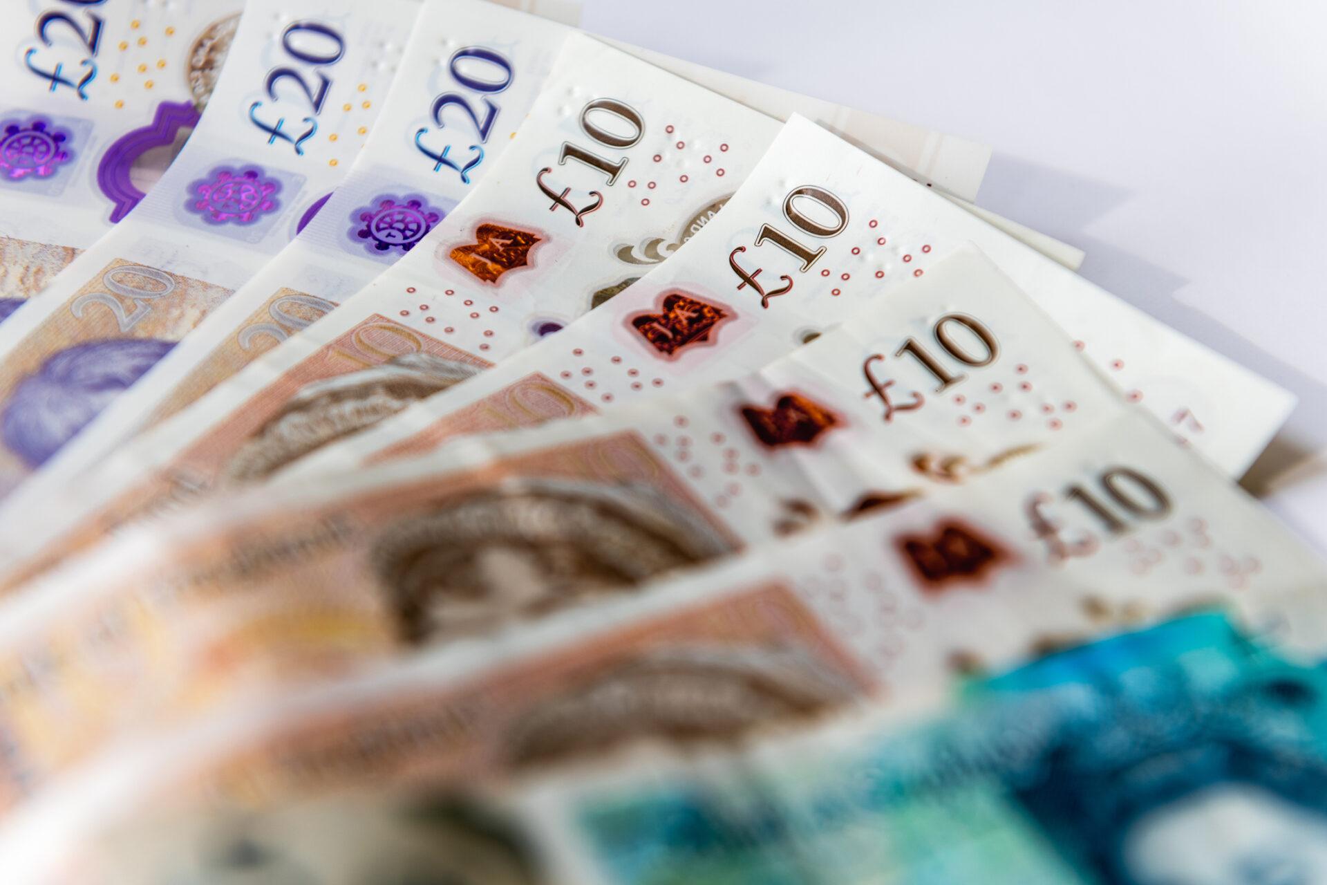 A fanned-out stack of British pound notes showcasing different denominations, including £10 and £20 bills.