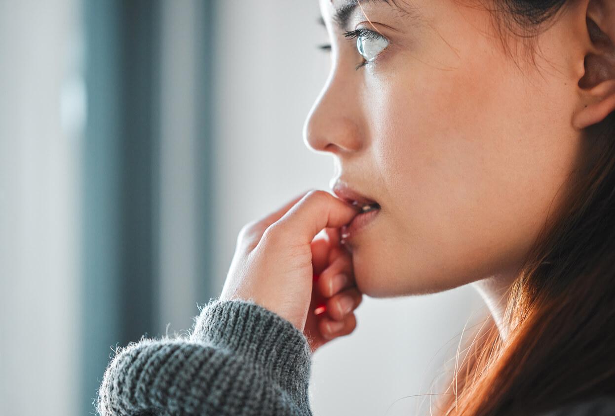 Female nervously biting her thumbnail as a result of feeling paranoid.