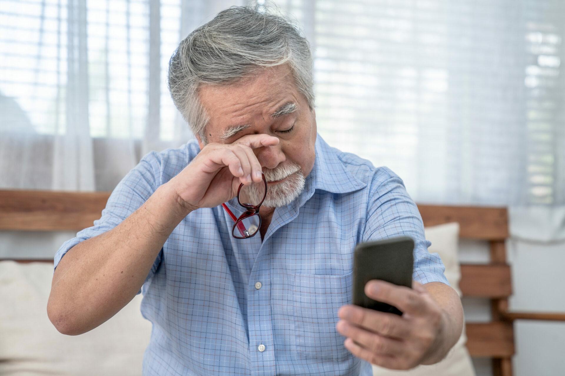 An older man scratching his eyes while struggling to look at phone display