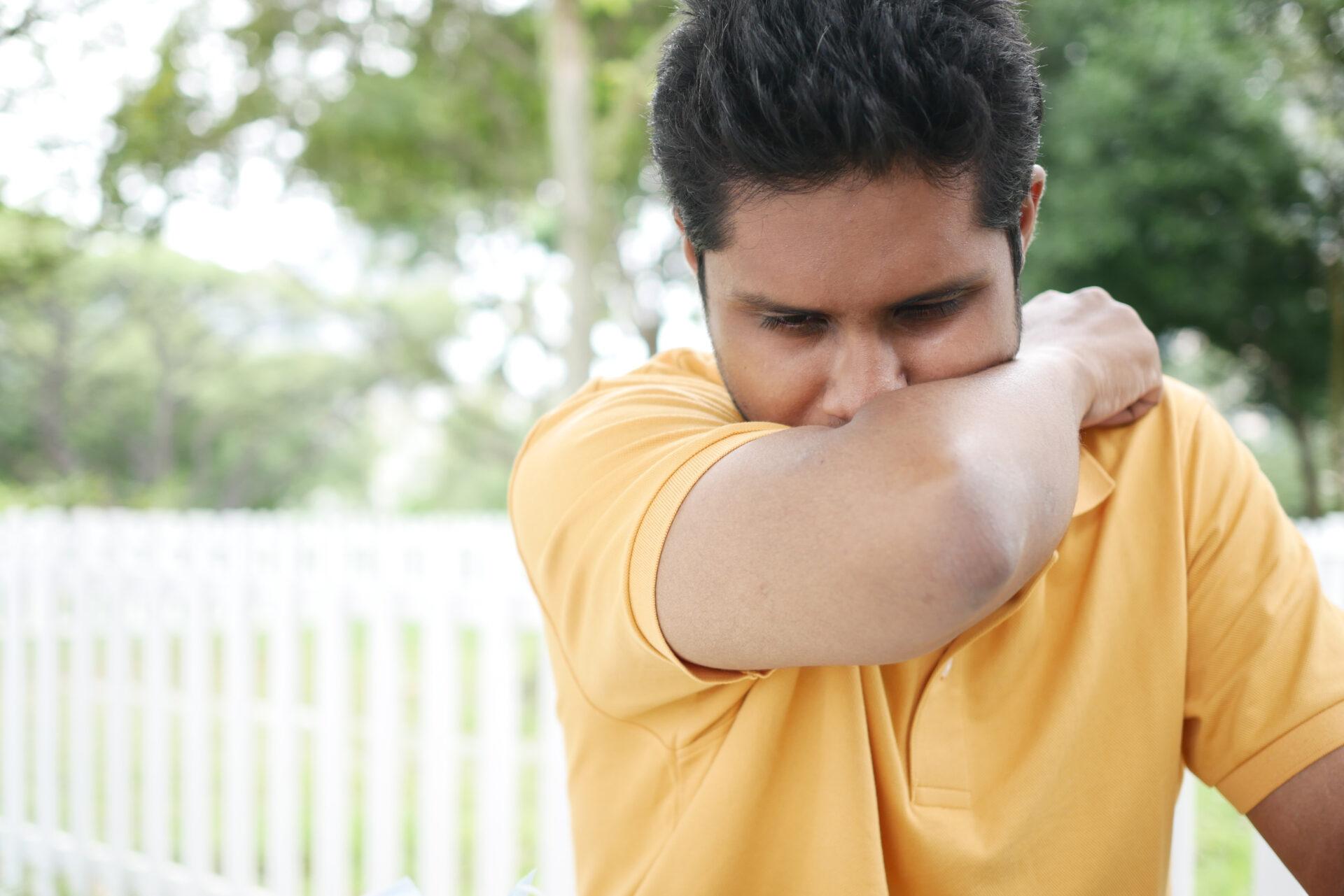 Young man using his arm to cover his nose and mouth.