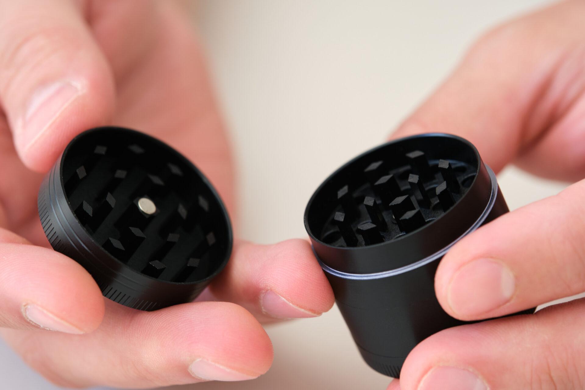 Two hands holding an empty marijuana grinder.