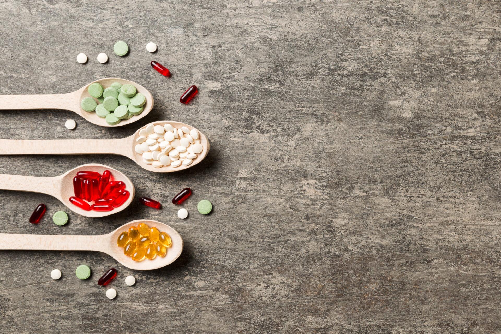 Variety of vitamin and mineral pills in wooden spoon on coloured background.