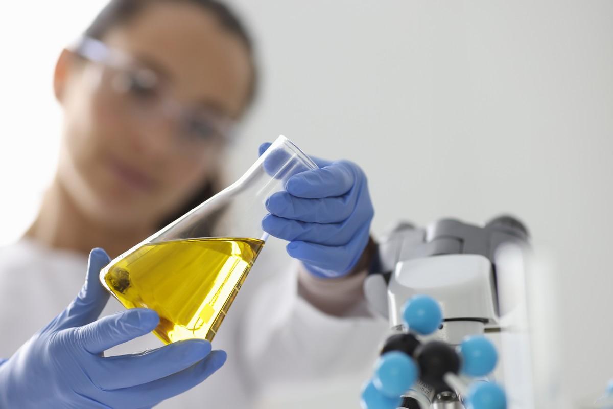 Close-up of a researcher holding a flask filled with a yellow fluid.