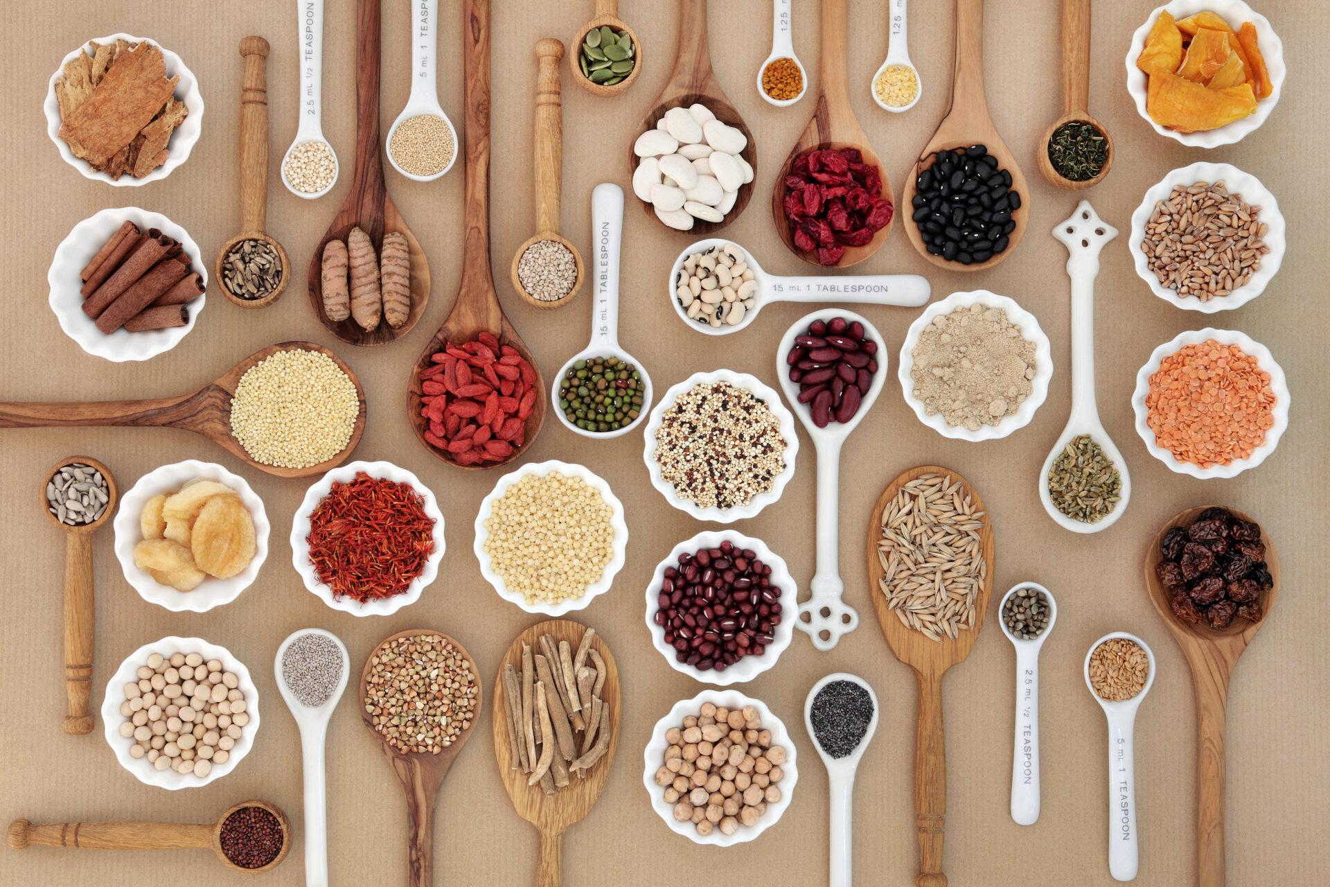 Spoons and bowls with vitamins and supplements on brown background.