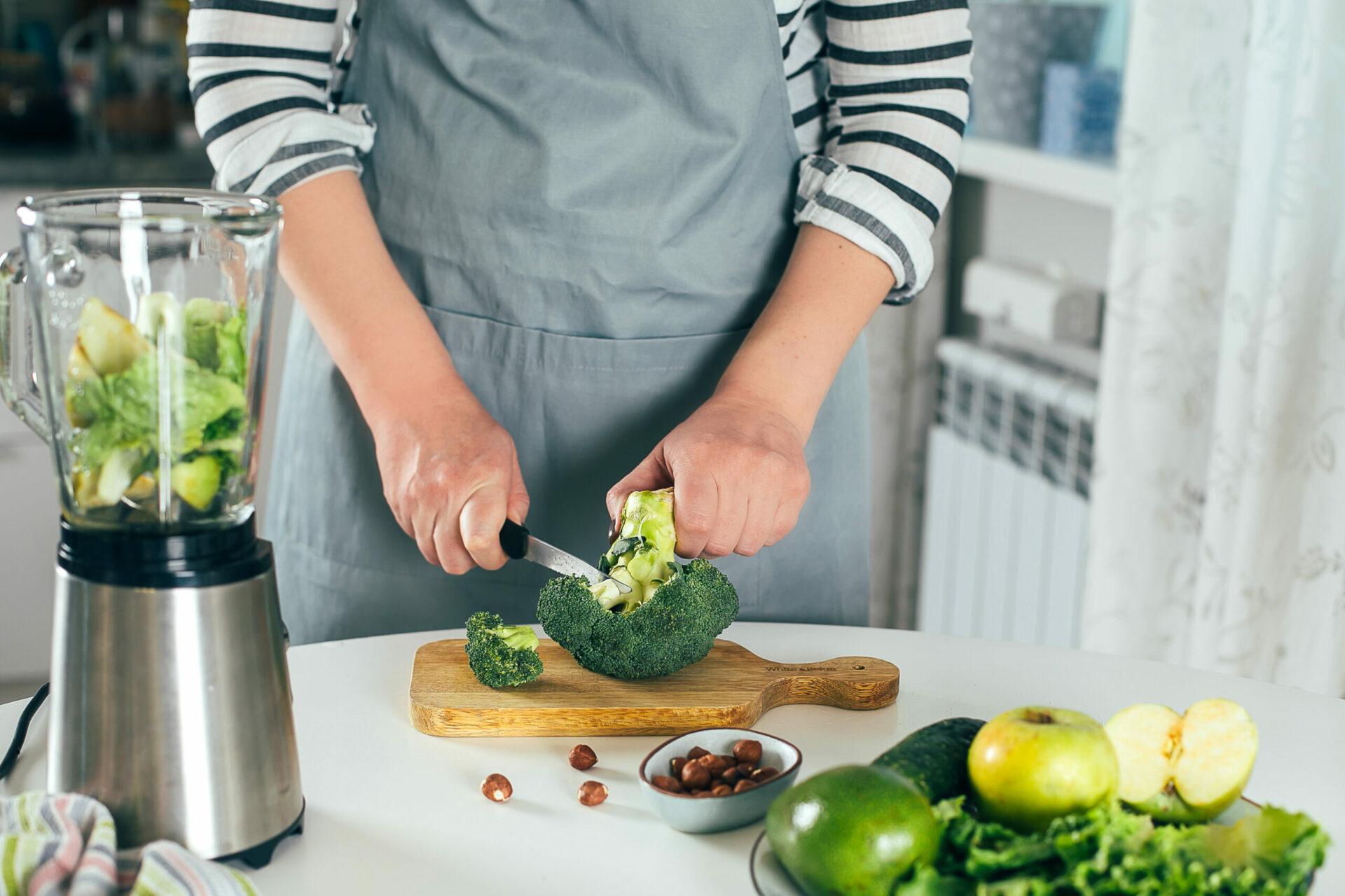 Woman cuts broccoli and makes healthy green smoothie.