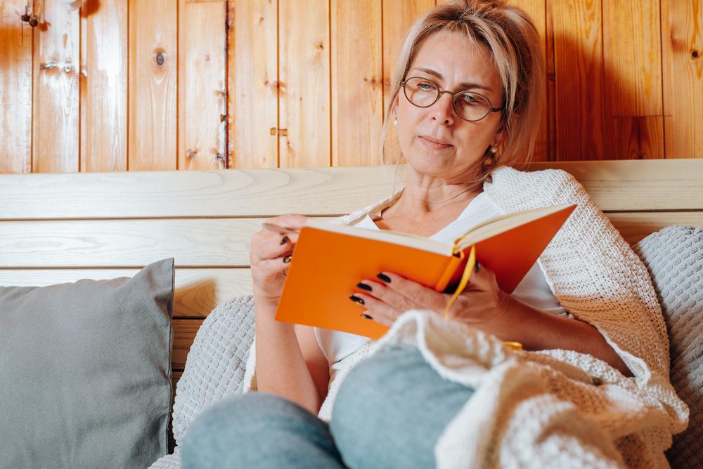 Close-up adult woman wearing glasses taking notes sitting on a bed