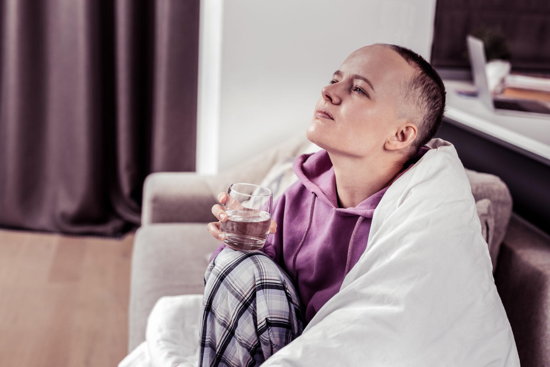 Female cancer patient holding a glass of water while sitting on a sofa.