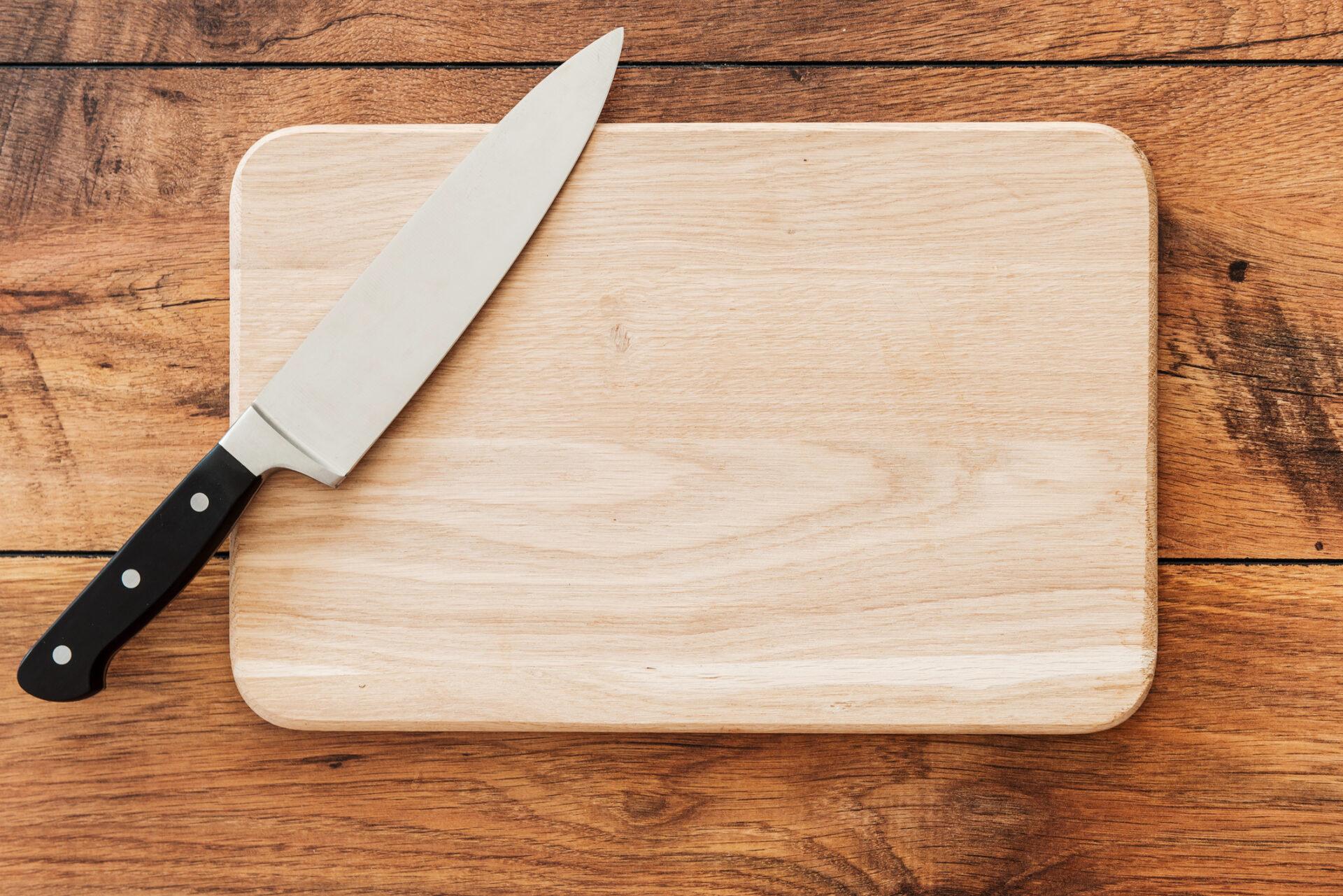 Top-down view of a knife resting on a wooden chopping board.