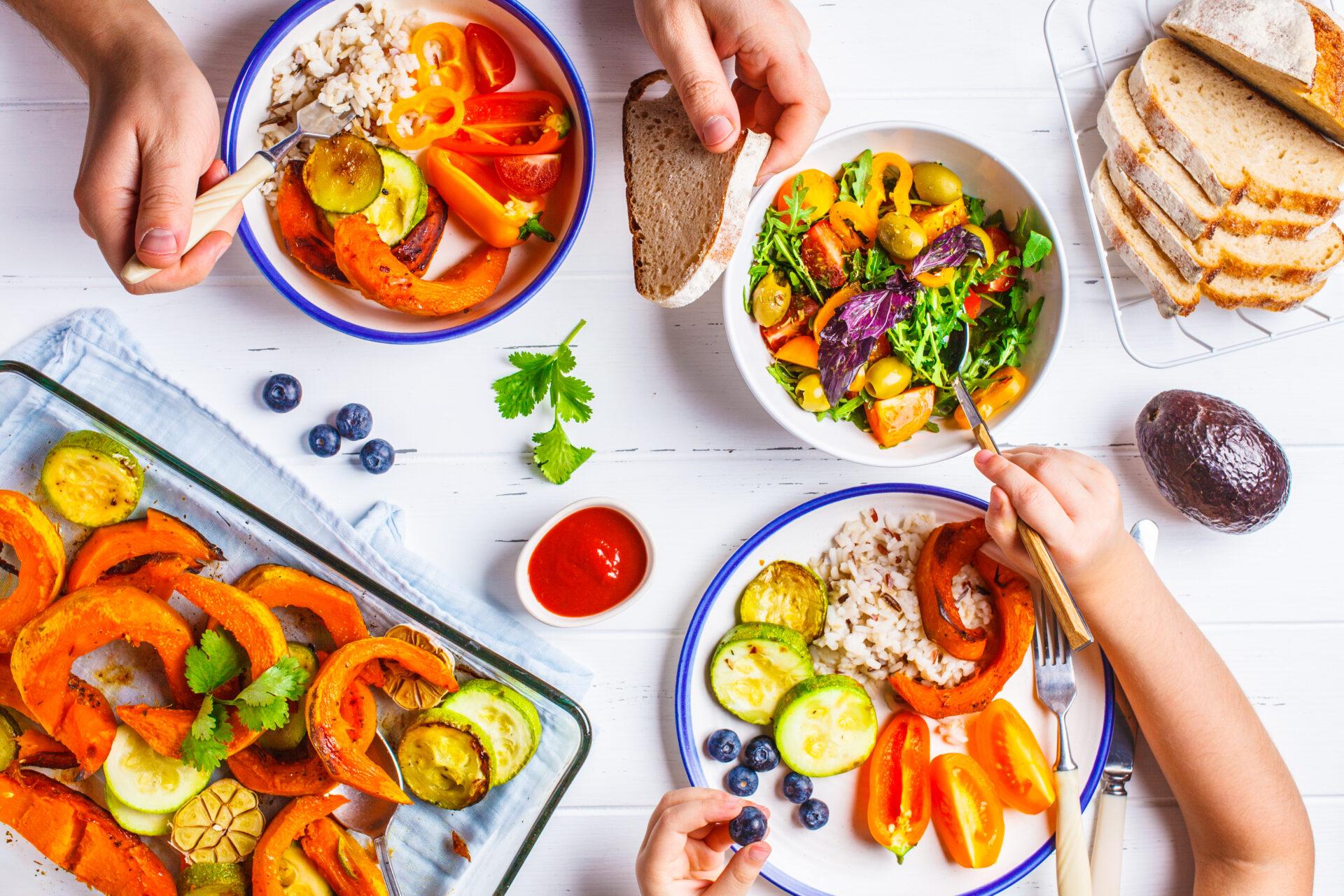 Flat lay of family hands eating healthy food. Baked vegetables, fresh salad, berries and bread on a white background.