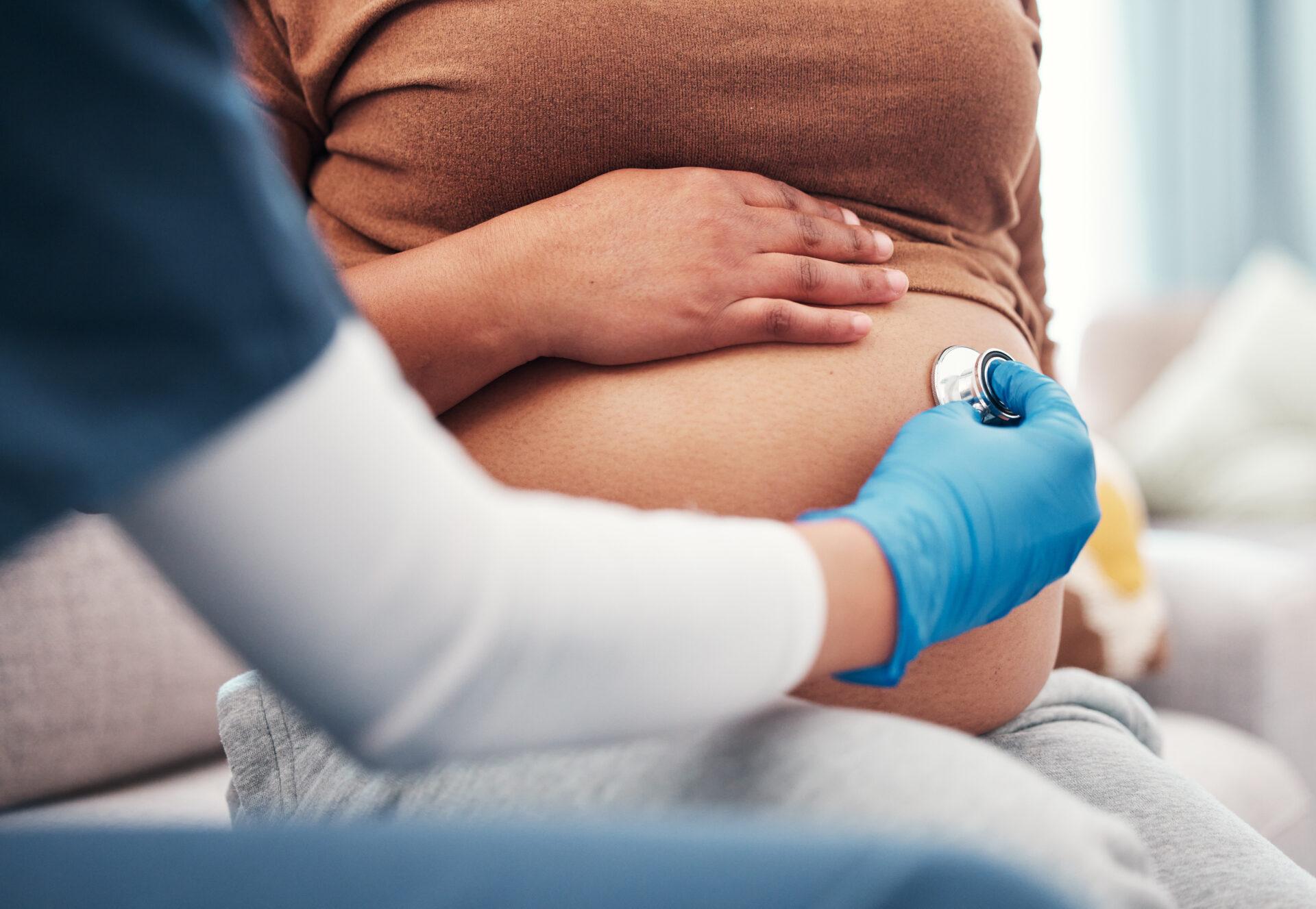 Close-up view of a nurse using a stethoscope on a pregnant mother's abdomen.