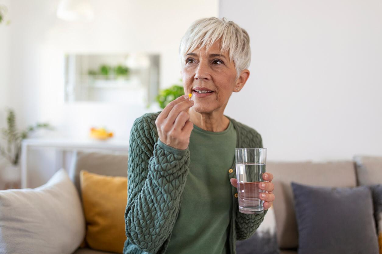 Senior woman takes a pill with a glass of water in hand.