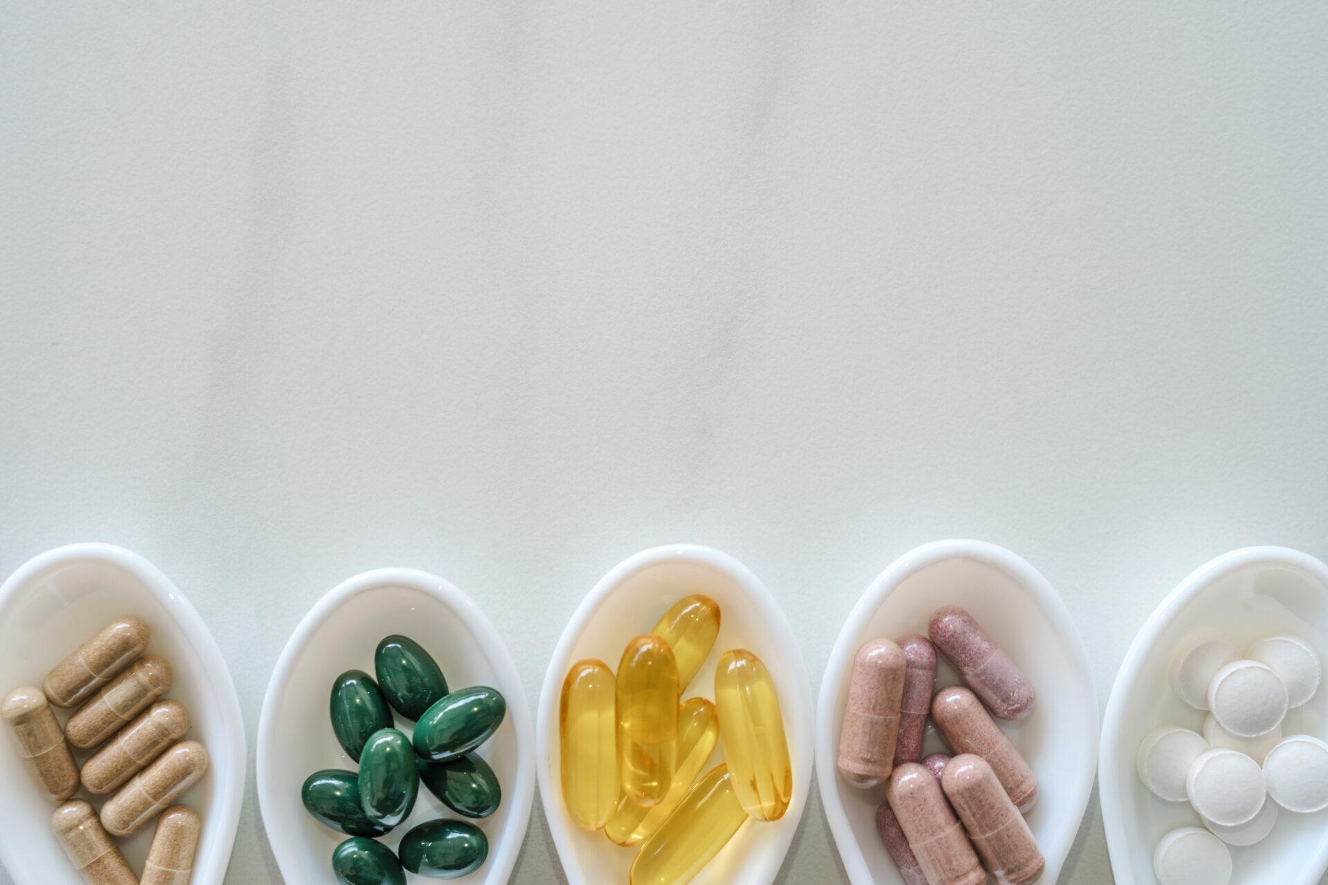 Supplements on white spoons on marble texture background.
