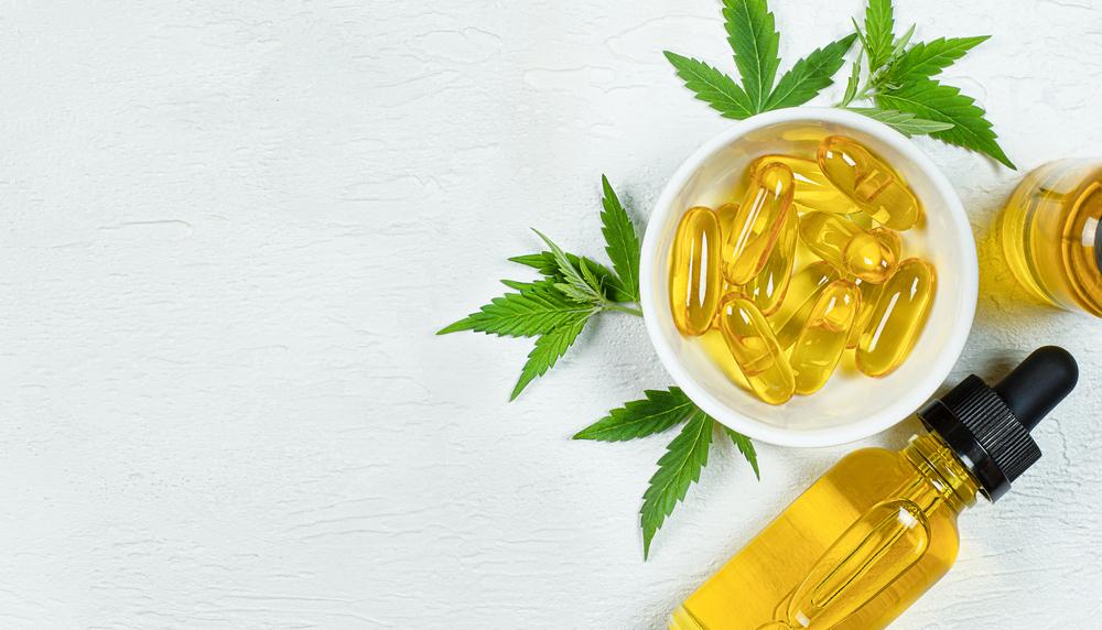 Cannabis oil, capsules and hemp leaves on a white surface