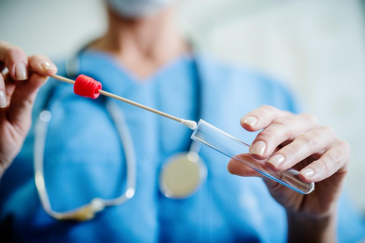 Close-up of medical professional preparing a test tube and swab for a saliva examination.