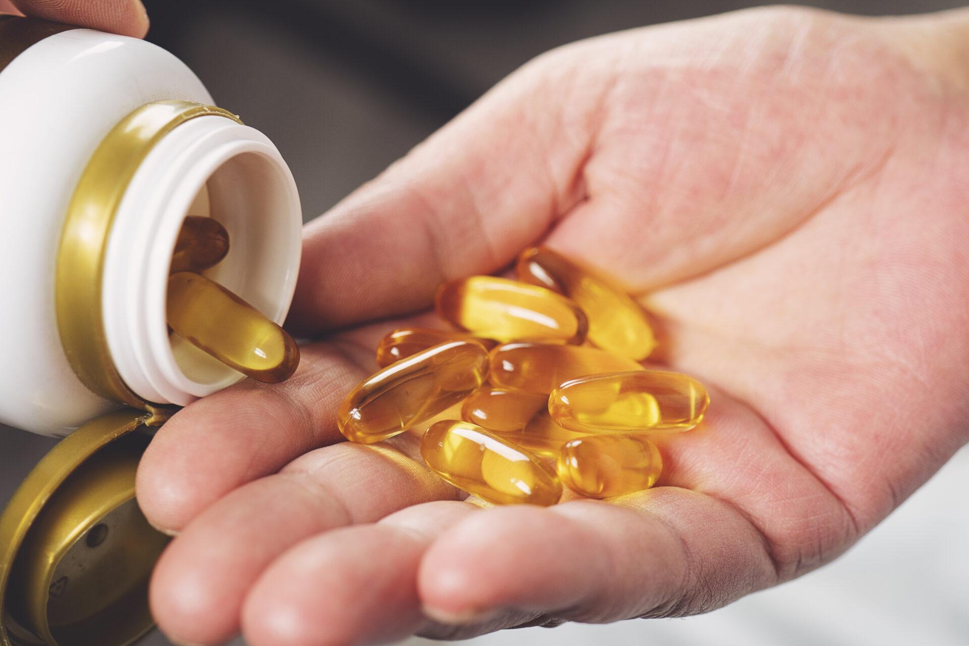 Hand pouring fish oil capsules from a bottle.