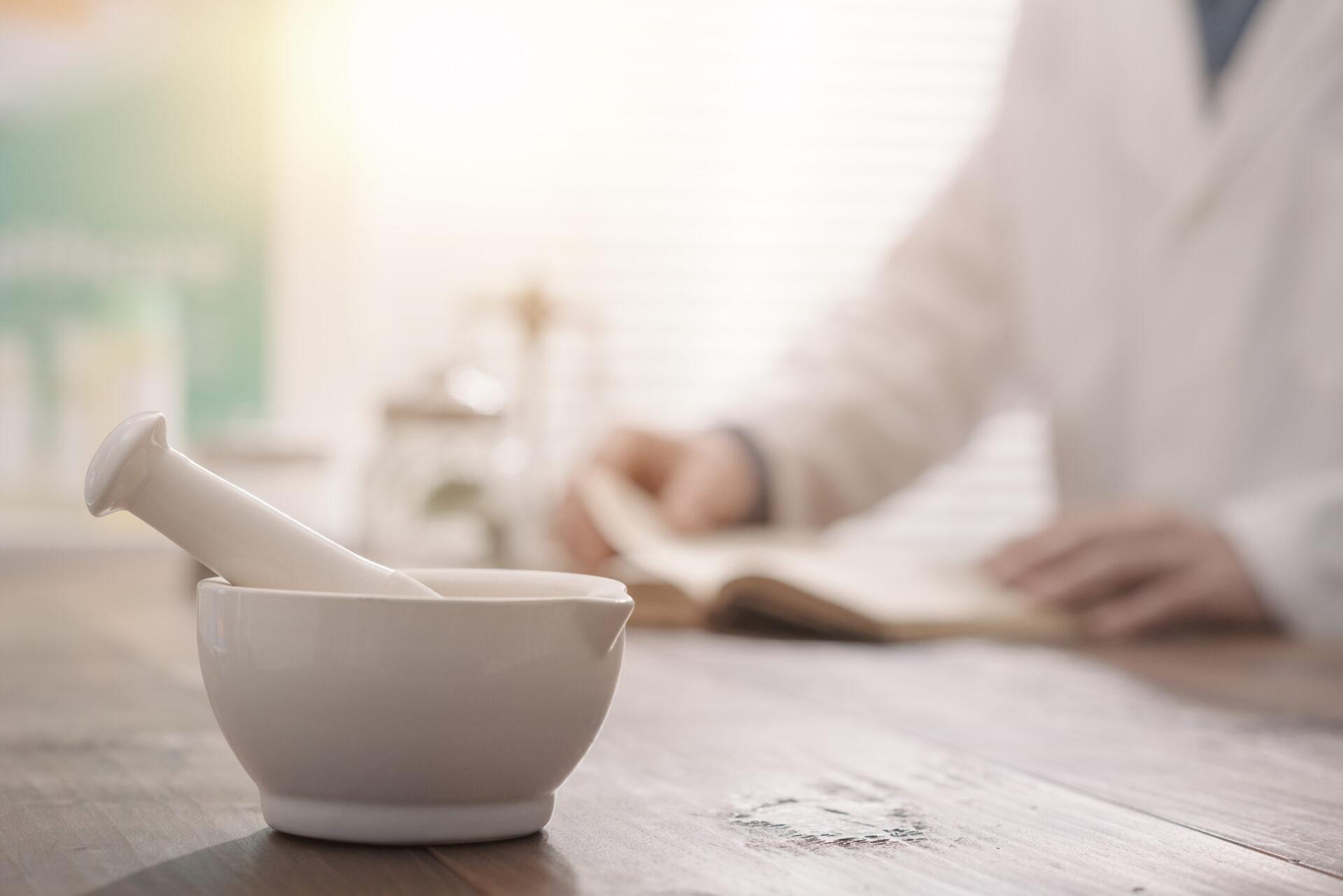 Close-up of a pestle and mortar, with a pharmacist visible in the background.
