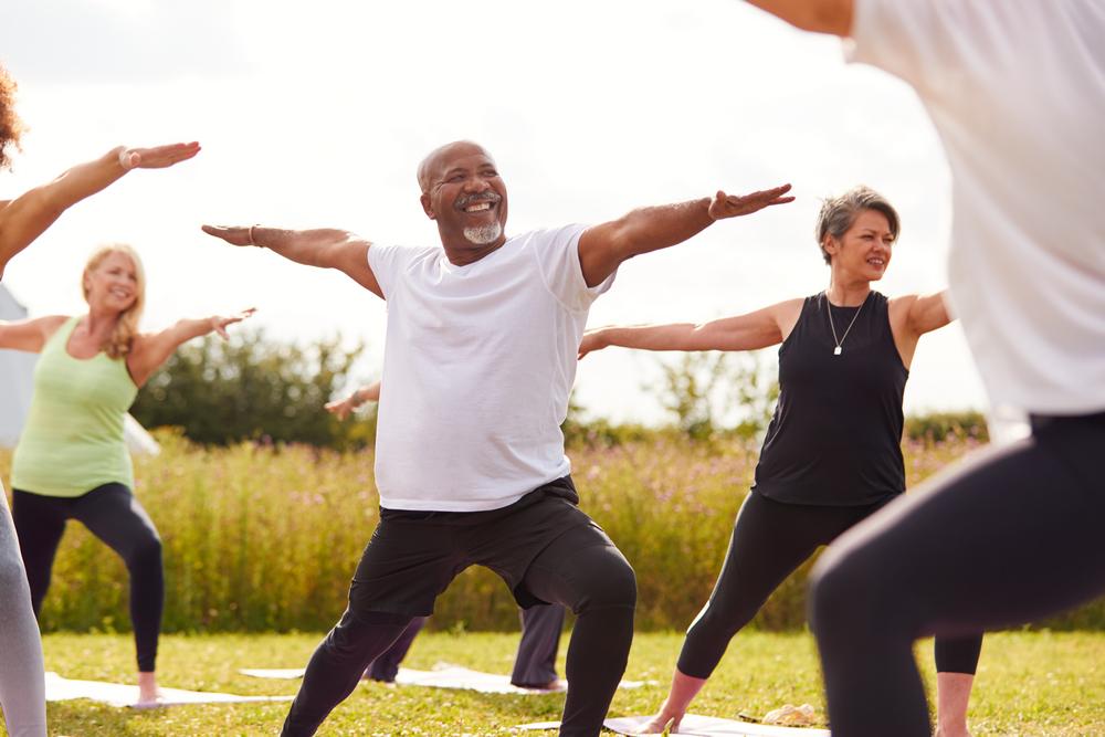 Female teacher leading group of mature men and women in class at outdoor yoga retreat