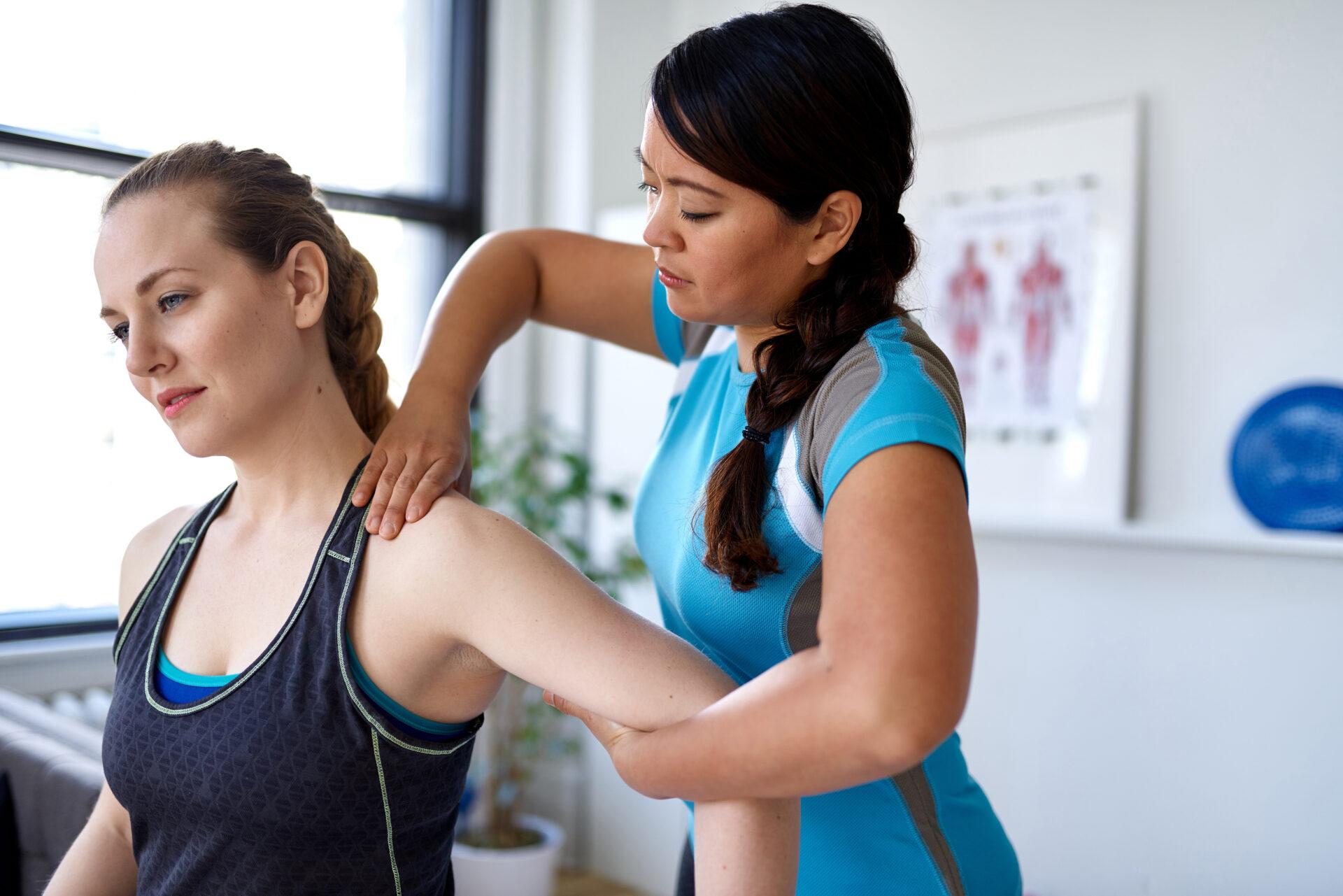 Female physiotherapy professional giving treatment to a female client in a bright medical office.