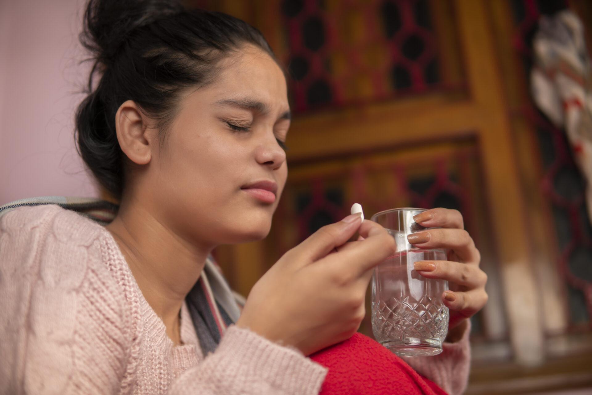 Anxious woman taking pills with a glass of water.