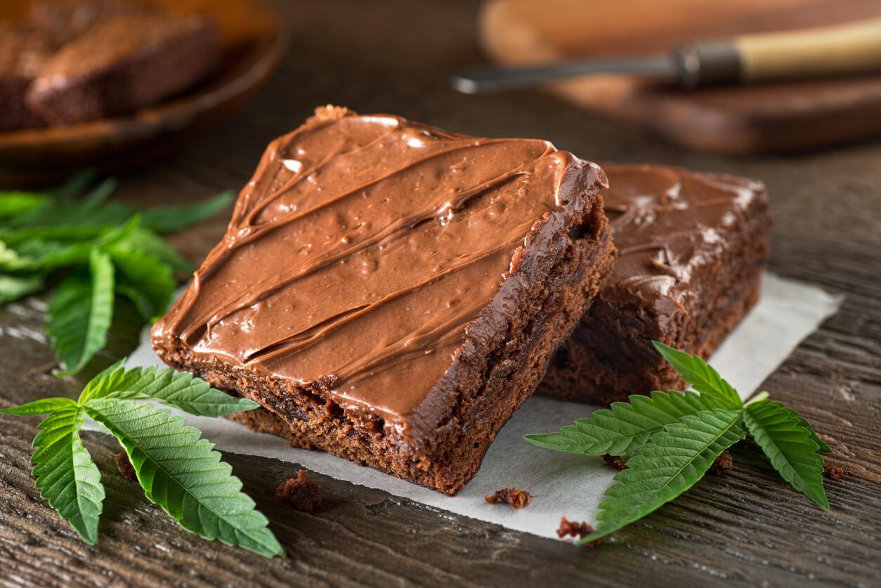 A rich chocolate brownie topped with glossy chocolate frosting, garnished with cannabis leaves, symbolising its infusion with cannabis extracts.