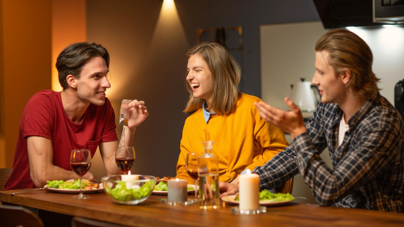 Three friends enjoy a lively conversation over dinner with wine in a cosy, warmly lit home setting. 
