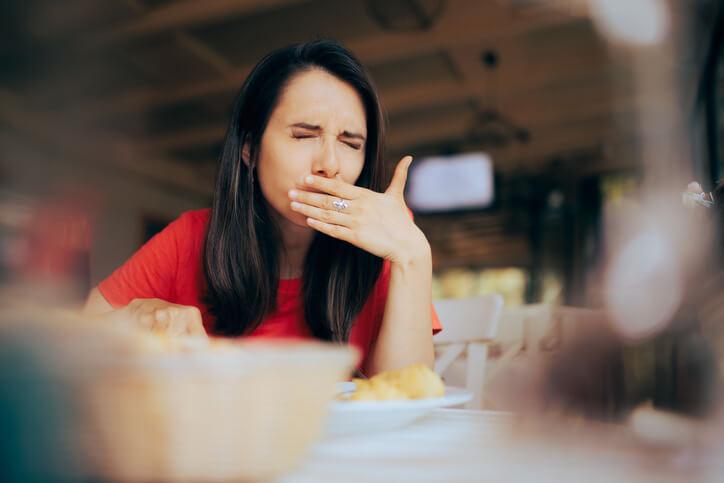 A woman feeling nauseous while eating at a restaurant, covering her mouth in discomfort.