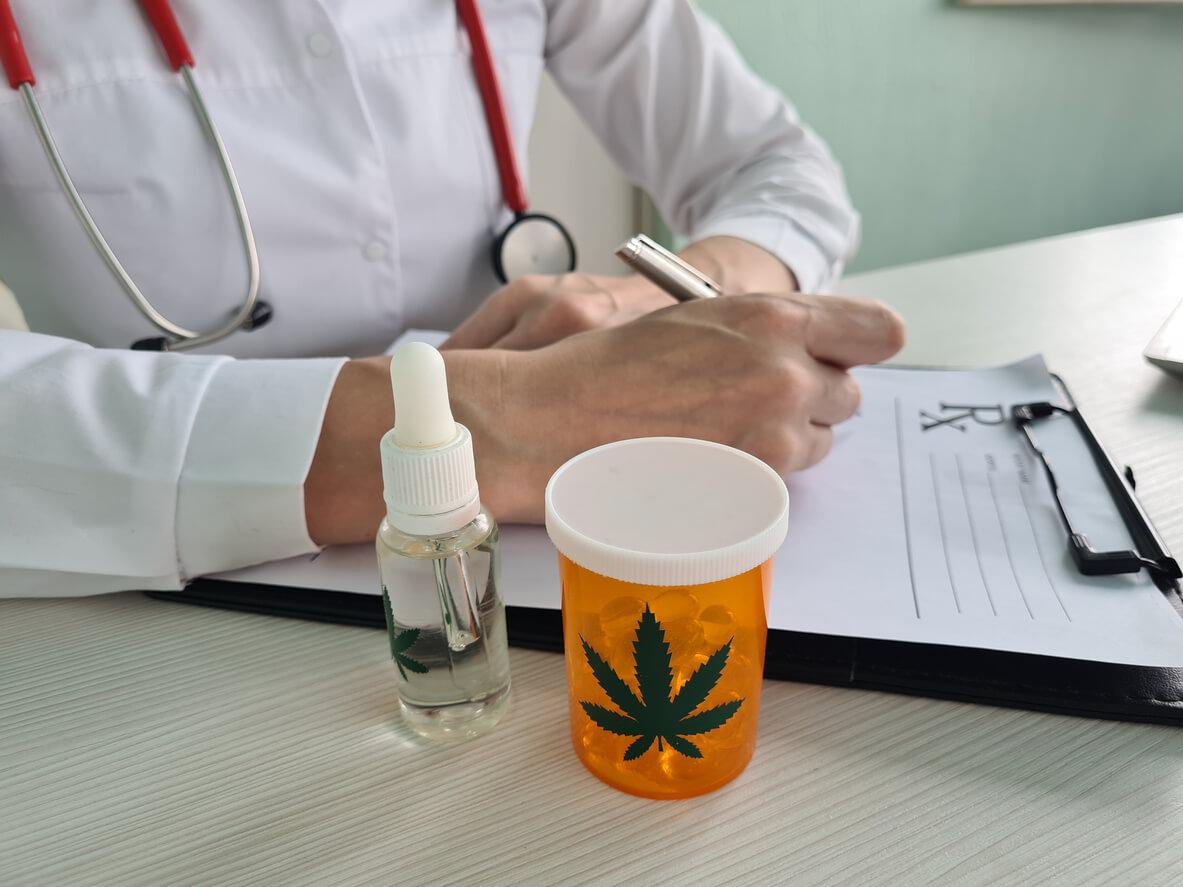 A doctor writing a prescription with a bottle of cannabis oil and a container of medical marijuana capsules on the table.