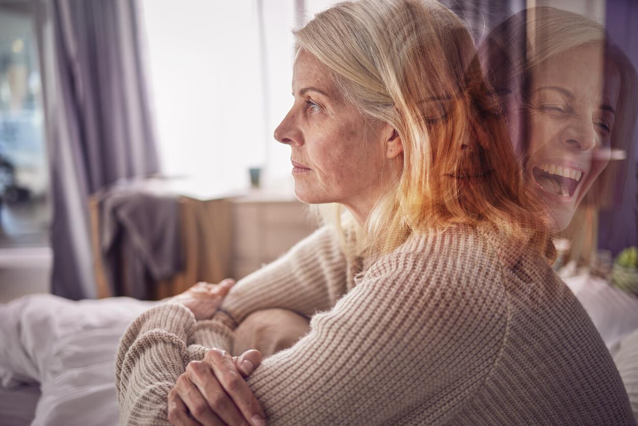 A middle-aged woman sitting on a sofa appears distressed. The image is layered with a transparent overlay of her in a contrasting emotional state, smiling and laughing, symbolising the contrasting moods experienced by individuals with bipolar disorder.